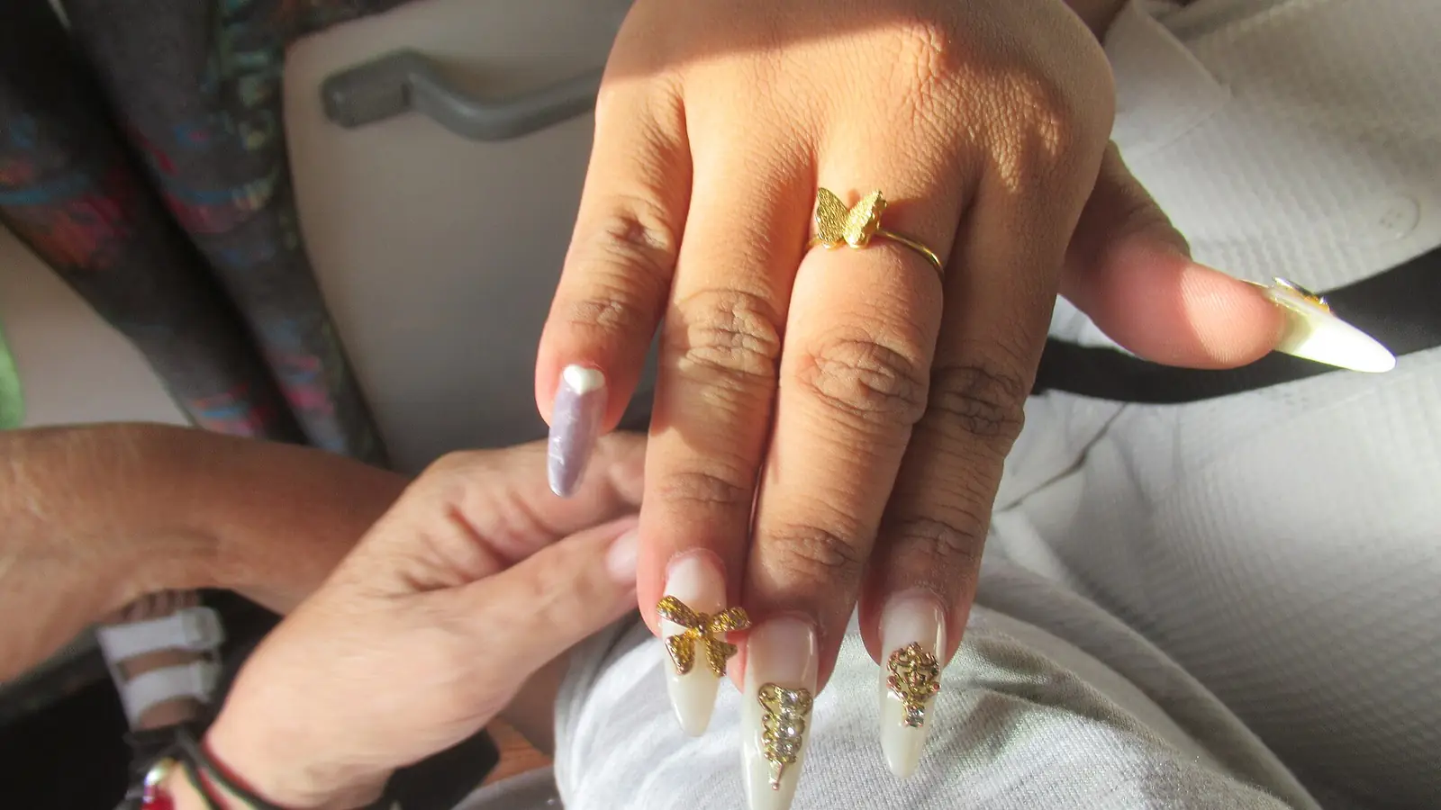 Long gold-tipped stiletto acrylic nails being finished by a nail technician