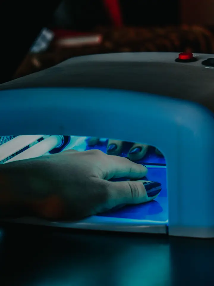 Hand under an LED nail lamp curing gel polish